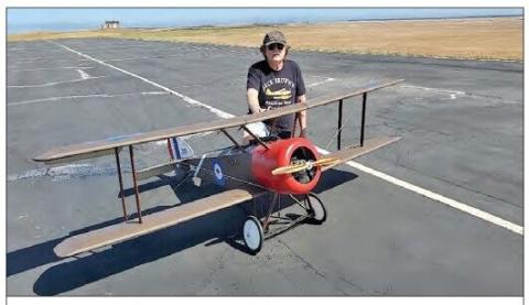 A large-scale Sopwith Pup model with its builder on an airport runway