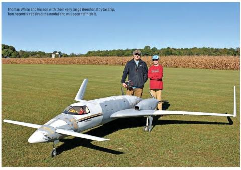 A very large RC Beechcraft Starship model on a grass field with Thomas White and his son standing behind it.
