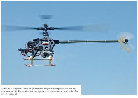 A Raptor 60/90 RC helicopter flying against a blue sky with its engine and related components removed.