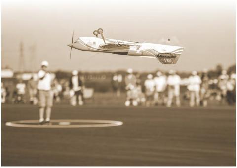 Radio-controlled model airplane flying above spectators at an outdoor event.