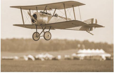 Sepia-toned biplane flying above a field.