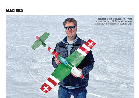 Man holding a green and white model Bf 109 airplane standing on snow.