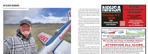 Man taking a selfie holding a large Corsair model on a grassy ridge with mountains in background