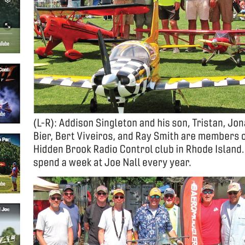 Group of men standing behind model airplanes on grass at event
