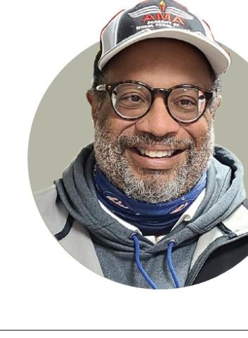 Headshot portrait of Randy Gibson smiling and wearing a cap and glasses