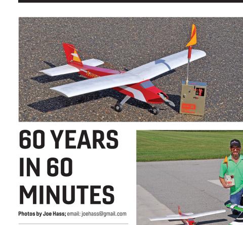 Red-and-white vintage model airplane sitting on pavement next to a remote and antenna flag