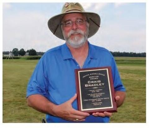 Craig Bradley standing outdoors holding an award plaque.