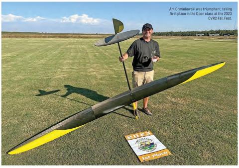 A man holds a radio-controlled sailplane and first-place award on a grassy field.