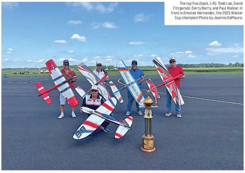 Five control line aerobatics competitors posing with model aircraft and a trophy on a runway.