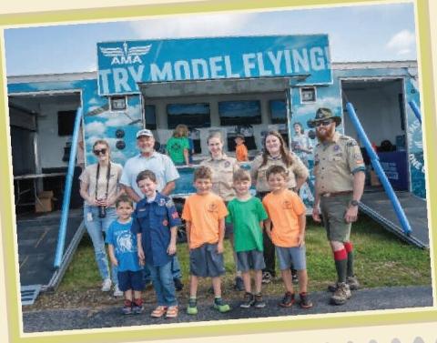 Children, adults, and a Boy Scout stand outside an AMA Try Model Flying facility.