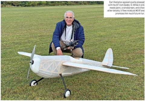 Carl Hampton kneeling behind a large translucent model airplane on a grassy field.