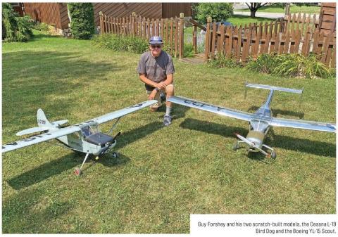 Guy Forshey seated behind two scratch-built model airplanes on a lawn.