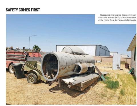 Beat-up mystery airplane fuselage on a trailer beside a fire truck at an air museum